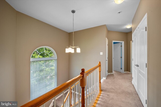 hallway with an upstairs landing, a chandelier, light carpet, and baseboards