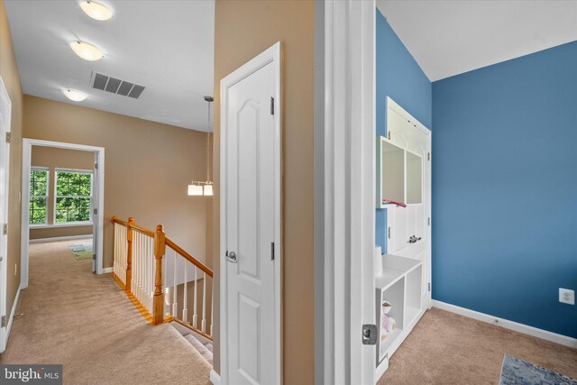 hall with an upstairs landing, carpet flooring, and baseboards
