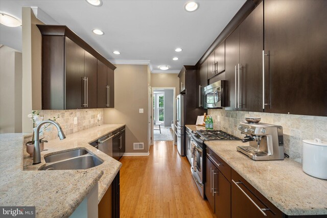 kitchen featuring appliances with stainless steel finishes, a sink, ornamental molding, recessed lighting, and light stone counters