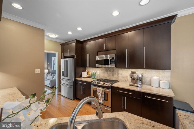 kitchen with stainless steel appliances, a sink, crown molding, decorative backsplash, and light wood-style floors