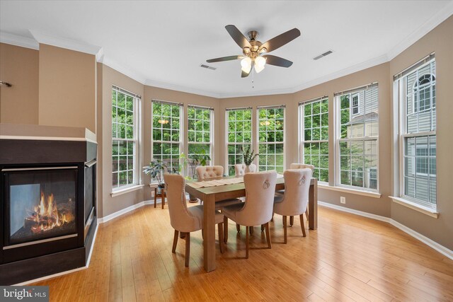 dining area with baseboards, a glass covered fireplace, light wood-type flooring, plenty of natural light, and crown molding
