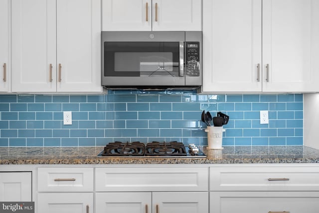 kitchen with white cabinets, gas stovetop, stainless steel microwave, and tasteful backsplash