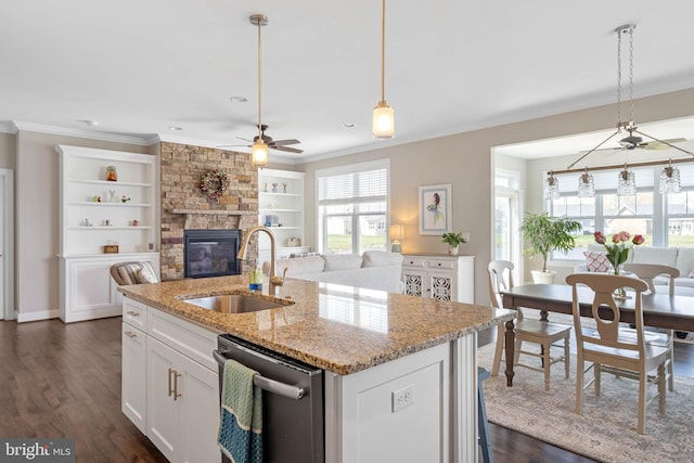 kitchen with a stone fireplace, stainless steel dishwasher, ornamental molding, a sink, and ceiling fan