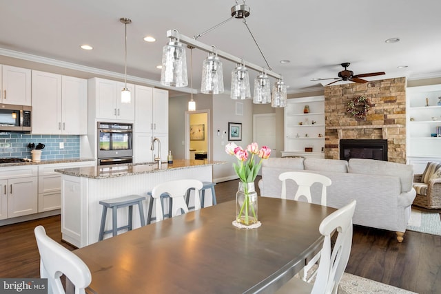 dining room with dark wood-type flooring, crown molding, a fireplace, and a ceiling fan