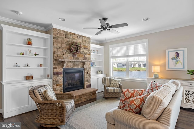 living area featuring ceiling fan, a stone fireplace, dark wood-type flooring, and ornamental molding