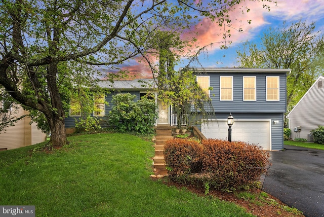 split level home with aphalt driveway, a front lawn, and an attached garage