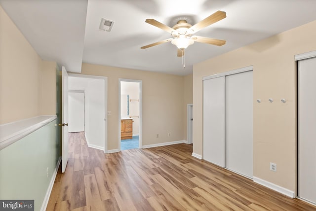 unfurnished bedroom featuring visible vents, baseboards, ensuite bathroom, light wood-style floors, and multiple closets