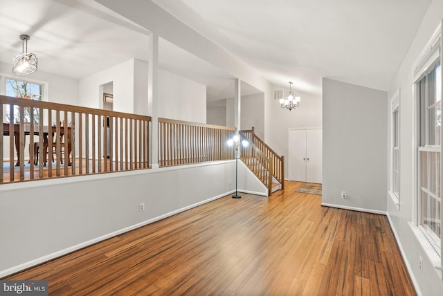 empty room featuring a chandelier, wood finished floors, and baseboards