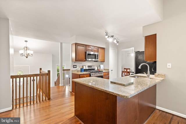 kitchen featuring a peninsula, light stone countertops, appliances with stainless steel finishes, light wood finished floors, and a sink