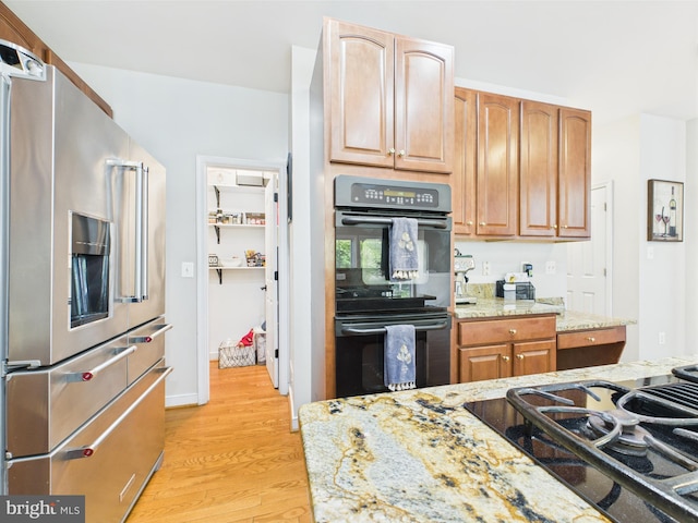 kitchen with black appliances, light stone countertops, and light wood finished floors