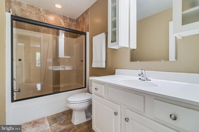 full bathroom with vanity, combined bath / shower with glass door, stone finish floor, and toilet