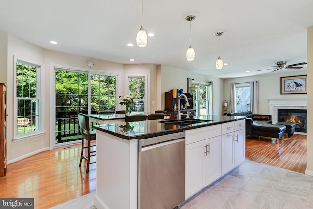 kitchen with a glass covered fireplace, a kitchen island with sink, a sink, dishwasher, and decorative light fixtures