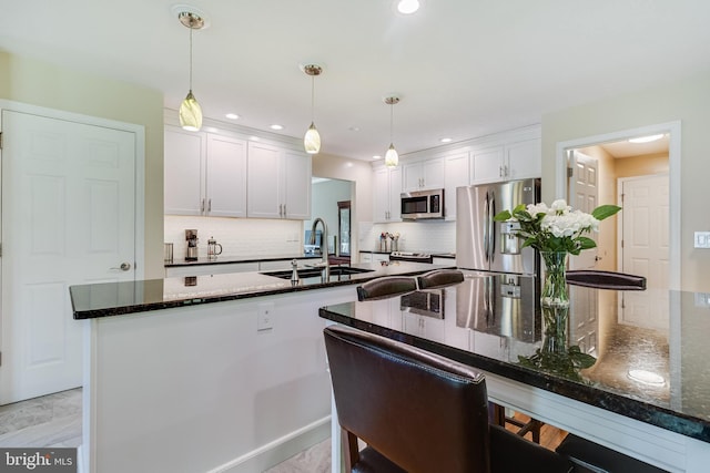 kitchen with white cabinets, a sink, stainless steel appliances, decorative backsplash, and pendant lighting