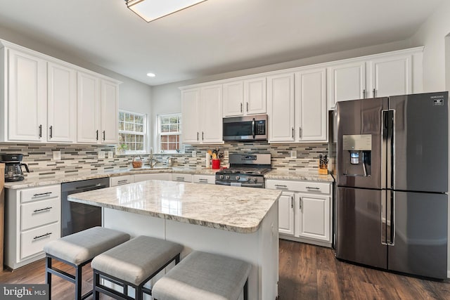 kitchen with appliances with stainless steel finishes, a sink, a breakfast bar area, white cabinetry, and recessed lighting
