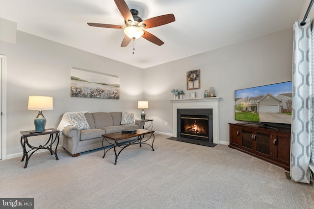 living area featuring a ceiling fan, baseboards, a fireplace with flush hearth, and light carpet