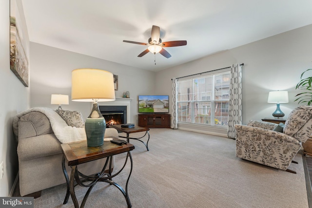 living area featuring light colored carpet, ceiling fan, and a lit fireplace