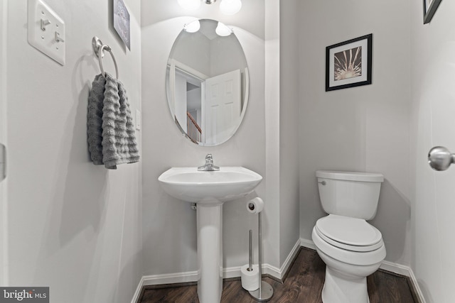 half bath with baseboards, a sink, wood finished floors, and toilet