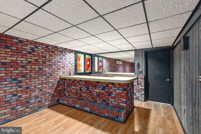 bar with a dry bar, a drop ceiling, wood finished floors, and brick wall