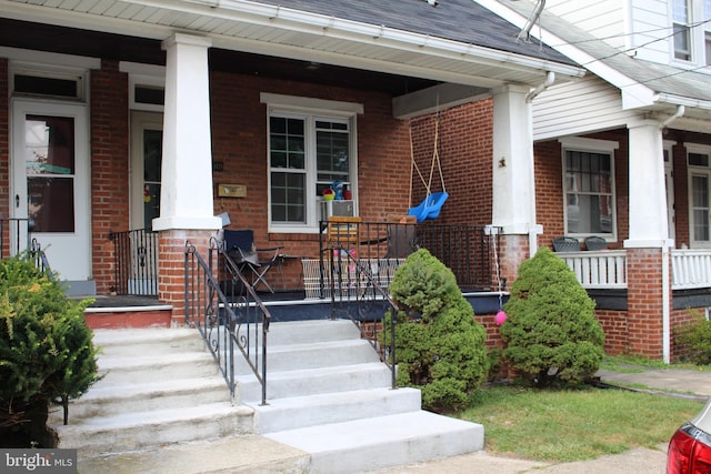 view of exterior entry with brick siding and covered porch