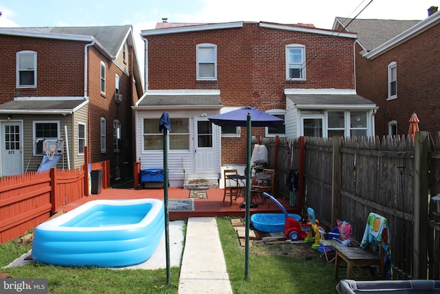 back of property with a swimming pool, a fenced backyard, a deck, and brick siding