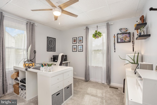 office area with healthy amount of natural light, ceiling fan, light carpet, a drop ceiling, and baseboards