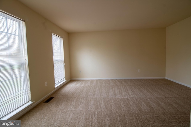 spare room featuring visible vents, baseboards, plenty of natural light, and light carpet