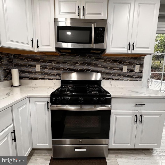 kitchen featuring light wood-type flooring, white cabinets, light stone counters, stainless steel appliances, and backsplash