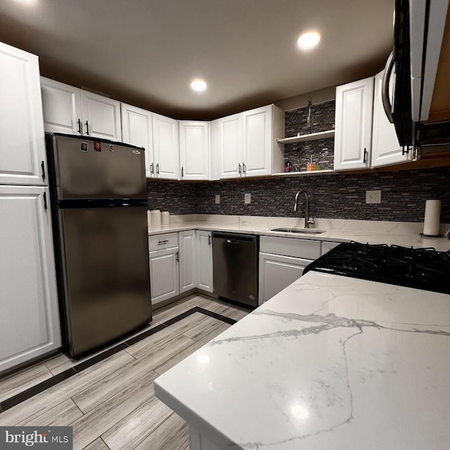 kitchen with freestanding refrigerator, open shelves, light stone counters, dishwasher, and a sink