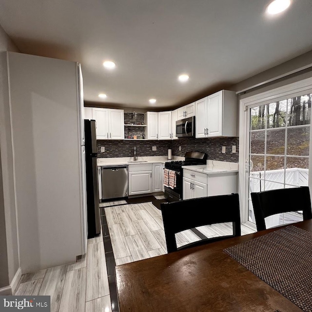 kitchen featuring tasteful backsplash, white cabinetry, open shelves, appliances with stainless steel finishes, and a sink