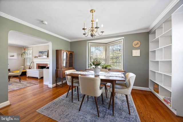 dining area featuring an inviting chandelier, wood finished floors, a fireplace, and crown molding
