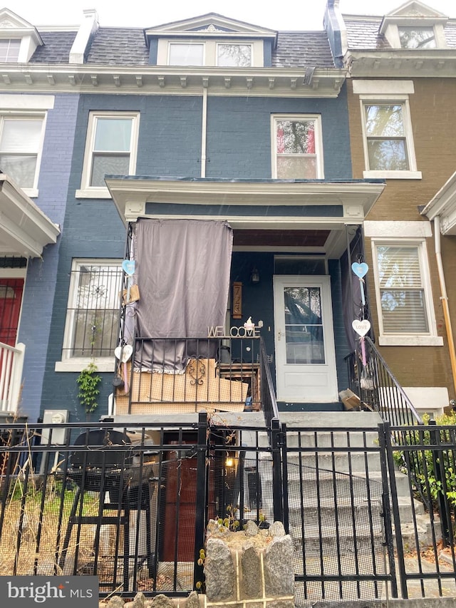 view of exterior entry featuring mansard roof, fence, and brick siding