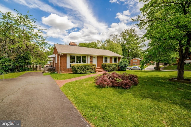 view of front of home featuring brick siding, driveway, a chimney, and a front yard