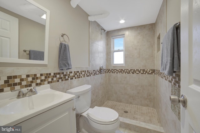 full bathroom with a tile shower, tile walls, toilet, and vanity