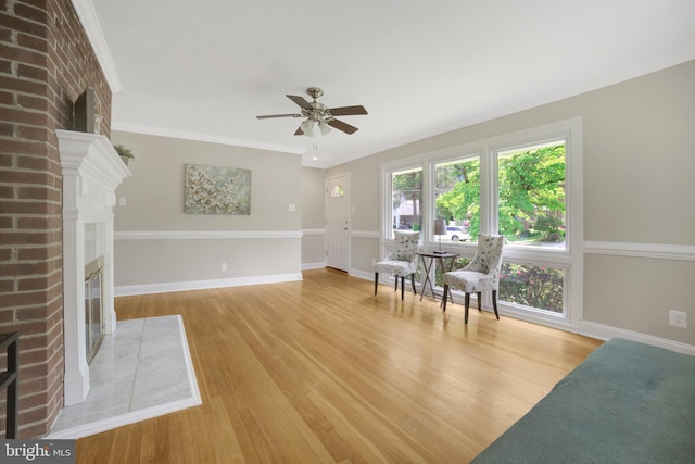 sitting room with a fireplace, ceiling fan, light wood-type flooring, baseboards, and ornamental molding