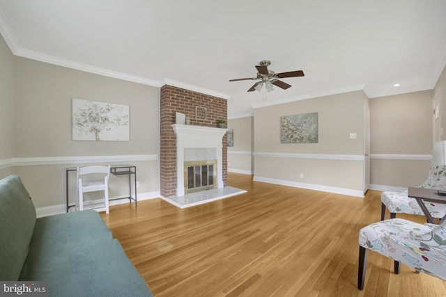 living room with ceiling fan, light wood-style floors, a fireplace, baseboards, and ornamental molding