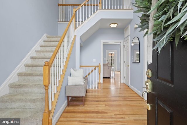 entrance foyer featuring light wood-style flooring, baseboards, stairs, and a high ceiling
