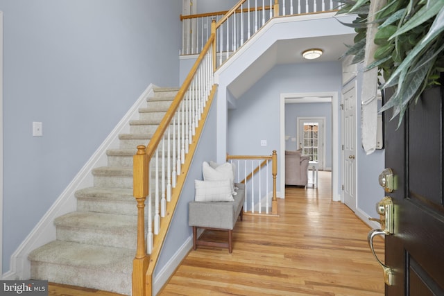 entryway with wood finished floors, baseboards, stairs, and a towering ceiling