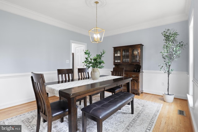 dining space featuring a chandelier, light wood finished floors, ornamental molding, and wainscoting