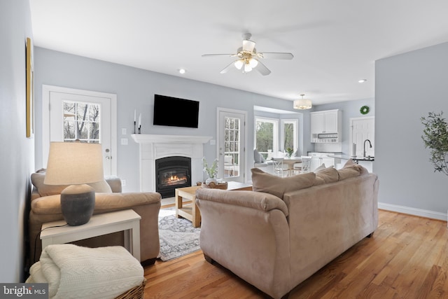living room with ceiling fan, a glass covered fireplace, light wood-type flooring, recessed lighting, and baseboards