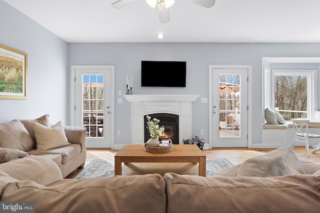 living room featuring ceiling fan, a glass covered fireplace, light wood finished floors, and baseboards
