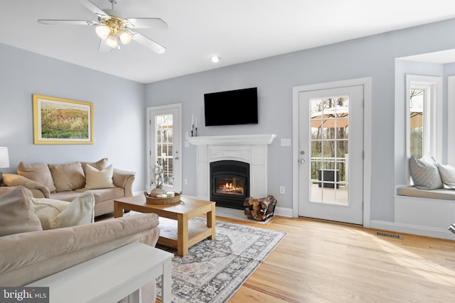living room featuring healthy amount of natural light, a glass covered fireplace, light wood-type flooring, and ceiling fan