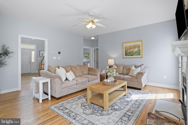 living area with a ceiling fan, light wood finished floors, baseboards, and a fireplace with flush hearth