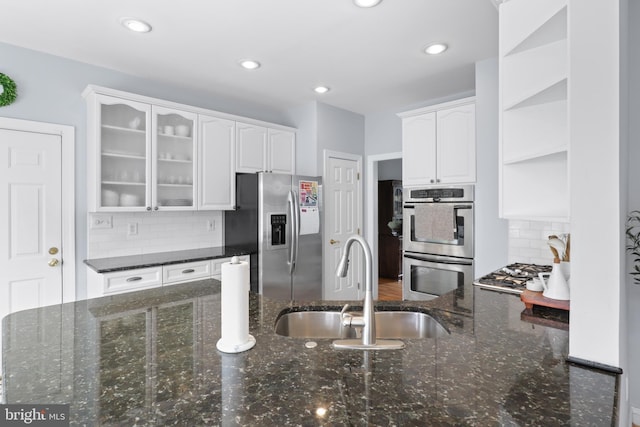 kitchen with appliances with stainless steel finishes, a sink, white cabinets, glass insert cabinets, and backsplash