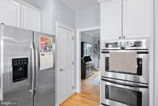 kitchen with stainless steel appliances, white cabinets, and light wood-style flooring
