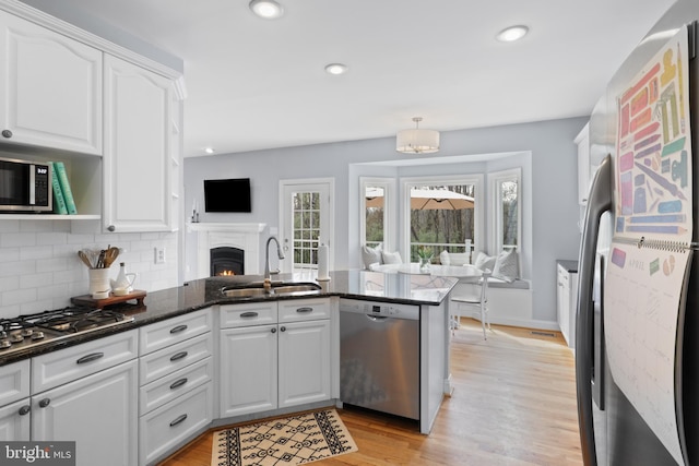 kitchen featuring appliances with stainless steel finishes, a sink, a peninsula, white cabinets, and recessed lighting