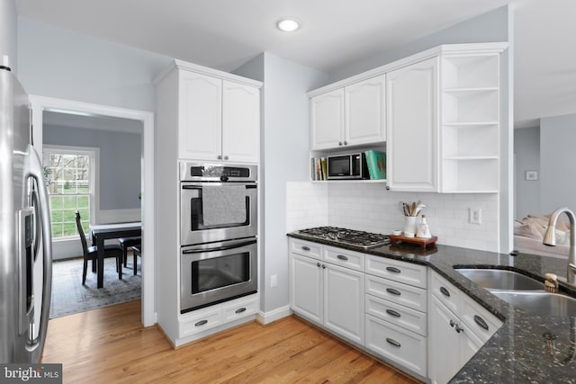 kitchen featuring stainless steel appliances, open shelves, white cabinetry, dark stone counters, and light wood-style floors