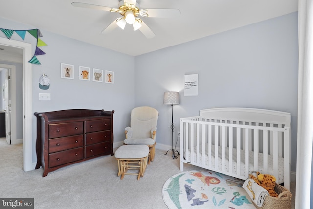 bedroom with a nursery area, carpet, a ceiling fan, and baseboards