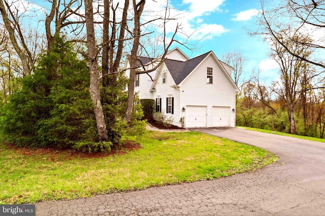 view of side of property with asphalt driveway, an attached garage, and a lawn