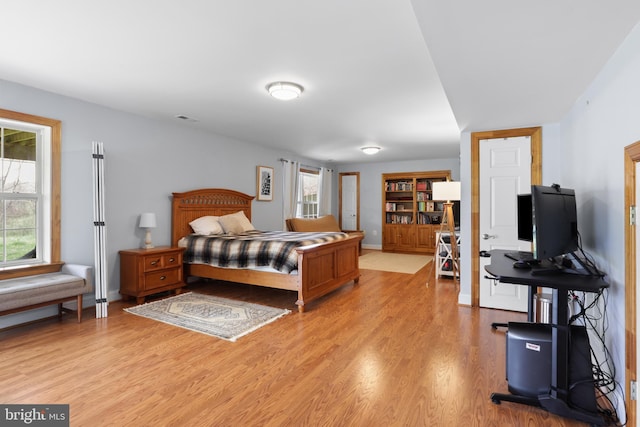 bedroom with multiple windows, light wood-type flooring, and baseboards