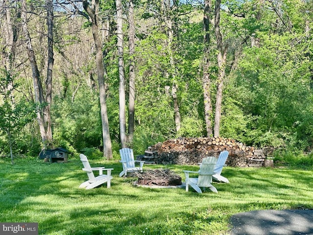 view of green lawn featuring a fire pit and a wooded view